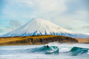 Surfeurs dans les îles Aléoutiennes avec le mont Vsevidof au loin-Chris Burkard Photography