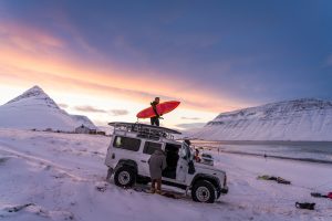 Un surfeur se tient sur un véhicule déchargeant sa planche de surf en Islande-Chris Burkard Photography